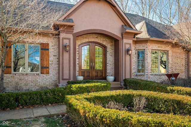 view of exterior entry featuring french doors, roof with shingles, and stucco siding