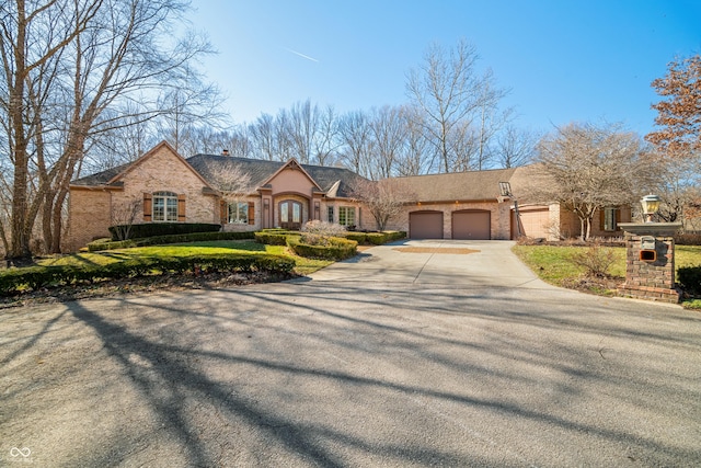 french provincial home featuring driveway, stone siding, an attached garage, and brick siding