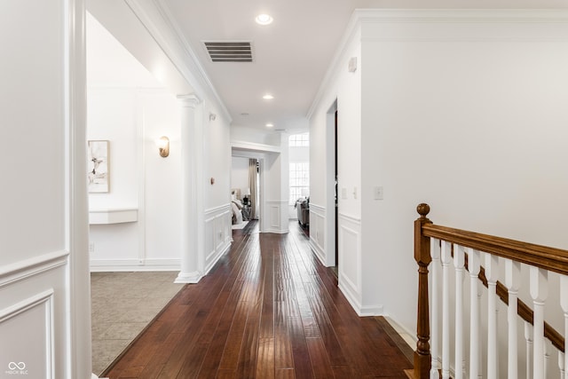 hallway with visible vents, crown molding, a decorative wall, and decorative columns