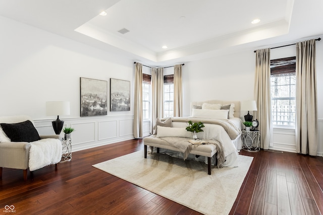 bedroom with visible vents, a raised ceiling, dark wood finished floors, and a decorative wall