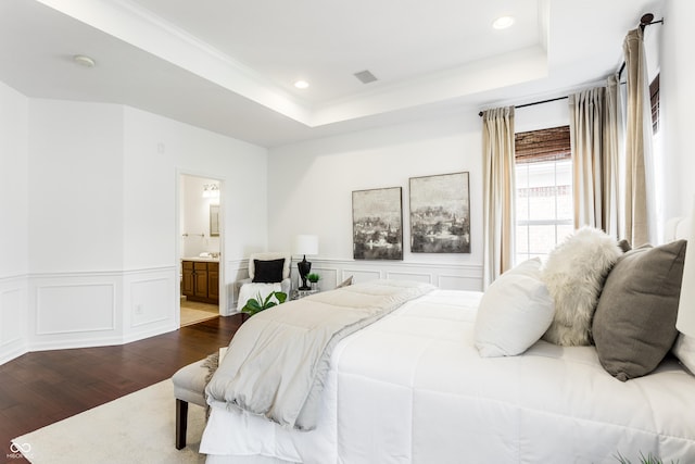 bedroom featuring a decorative wall, a wainscoted wall, a tray ceiling, and dark wood-style flooring