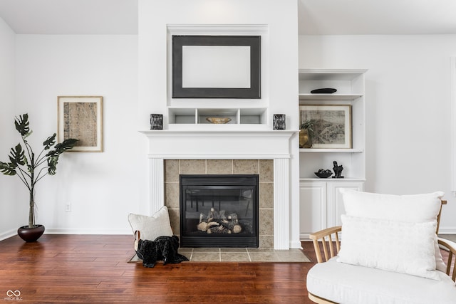 living area featuring built in shelves, a tile fireplace, baseboards, and wood finished floors