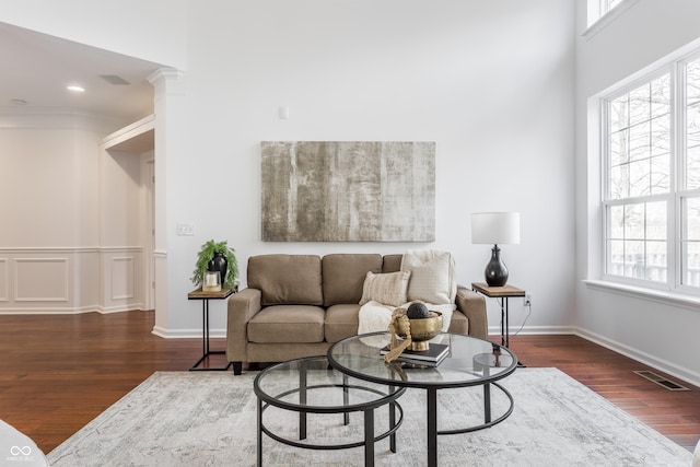 living area featuring visible vents, baseboards, ornamental molding, wood finished floors, and ornate columns