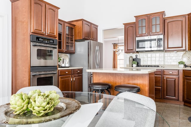 kitchen with a breakfast bar, light countertops, appliances with stainless steel finishes, backsplash, and a center island