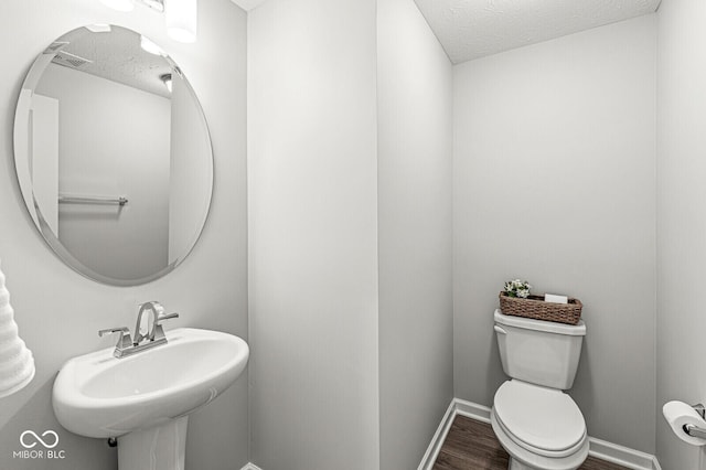 bathroom with toilet, a textured ceiling, baseboards, and wood finished floors