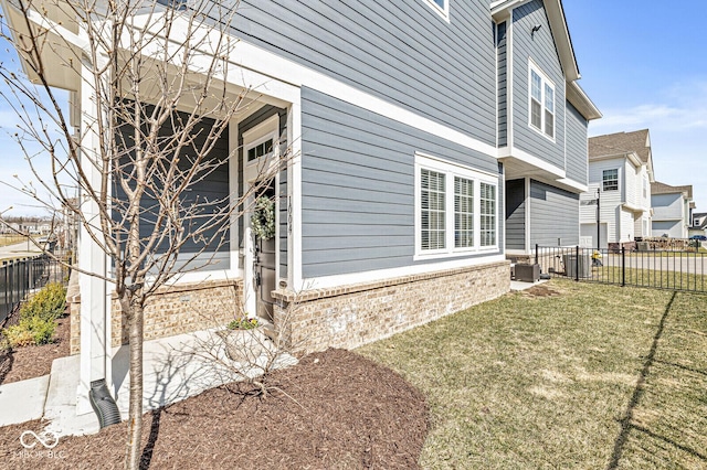 view of side of property featuring central AC unit, fence, brick siding, and a lawn