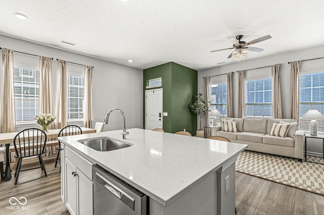 kitchen featuring light stone counters, light wood finished floors, ceiling fan, a sink, and dishwasher