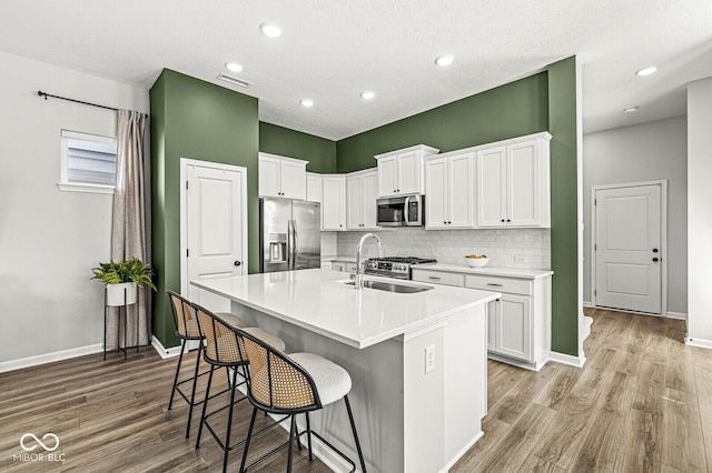 kitchen with visible vents, light wood-style flooring, a sink, backsplash, and stainless steel appliances