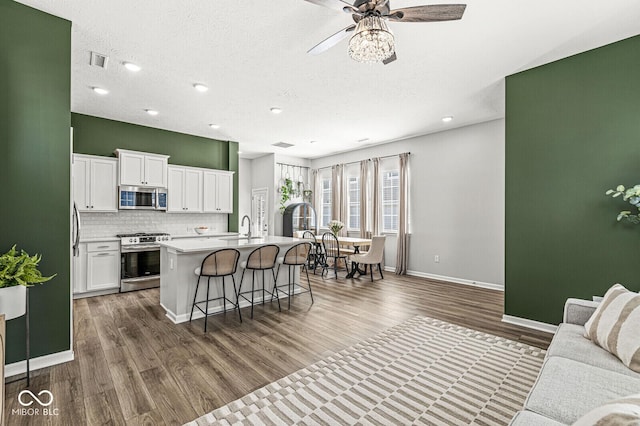 kitchen featuring a kitchen bar, a center island with sink, a sink, backsplash, and appliances with stainless steel finishes