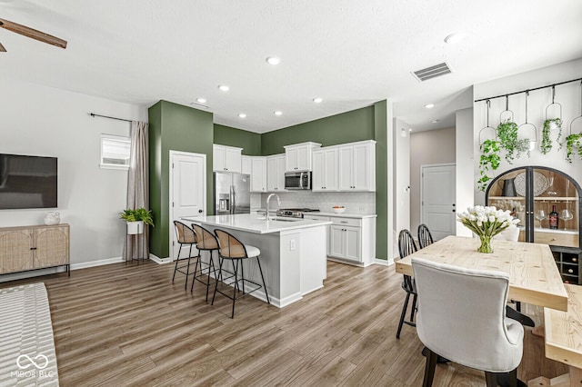 kitchen with a sink, stainless steel appliances, a kitchen island with sink, and light wood finished floors