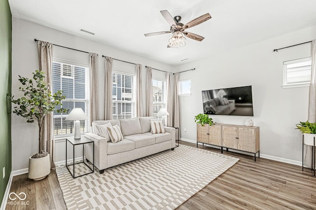 living room featuring visible vents, a ceiling fan, baseboards, and wood finished floors