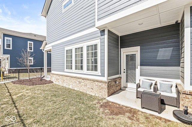 view of exterior entry with brick siding, a yard, and fence