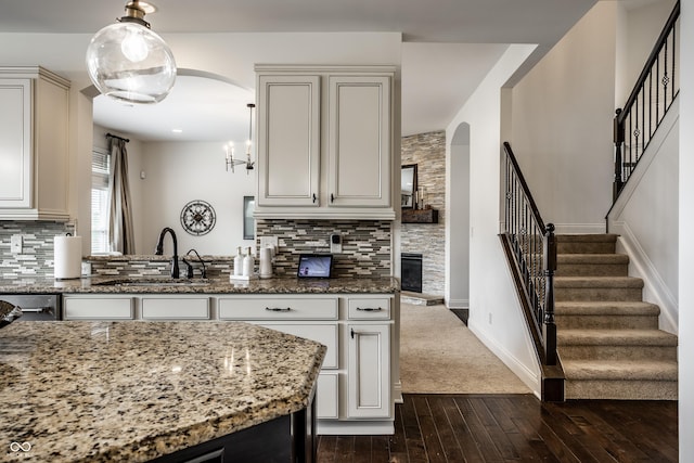 kitchen with a sink, arched walkways, backsplash, and dark wood-style floors