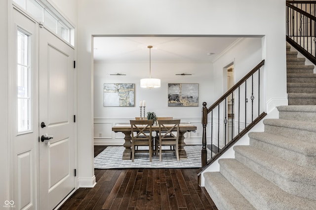 foyer entrance with stairs, dark wood-style flooring, ornamental molding, and a wainscoted wall