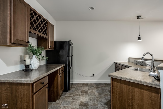 kitchen with dark brown cabinetry, a sink, freestanding refrigerator, baseboards, and pendant lighting