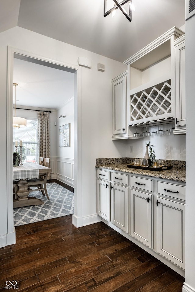 bar featuring dark wood-style flooring, a decorative wall, and wainscoting