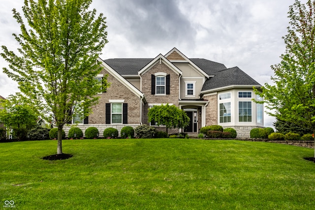 view of front of property with brick siding, a front lawn, roof with shingles, and stone siding