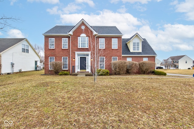 colonial-style house with a shingled roof, a front yard, and brick siding