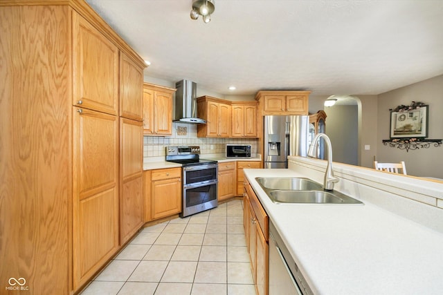 kitchen with light tile patterned floors, stainless steel appliances, light countertops, wall chimney range hood, and a sink