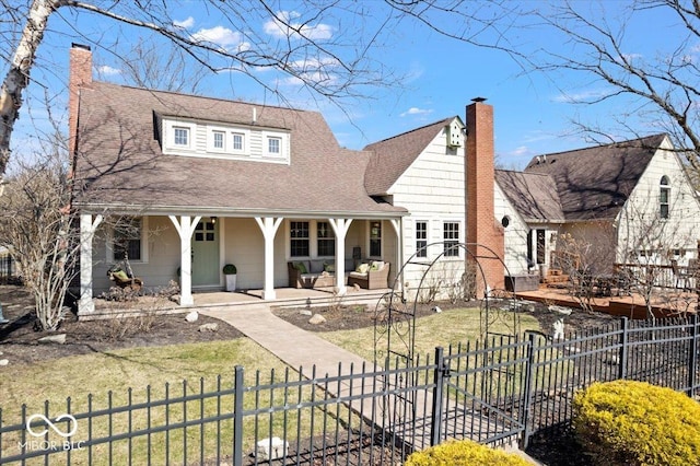 view of front of house with a fenced front yard, a porch, a chimney, and a front lawn