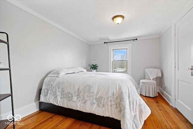 bedroom featuring visible vents, a textured ceiling, crown molding, light wood finished floors, and baseboards