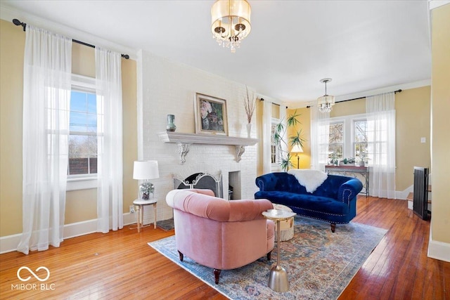 living room with hardwood / wood-style floors, an inviting chandelier, crown molding, baseboards, and a brick fireplace