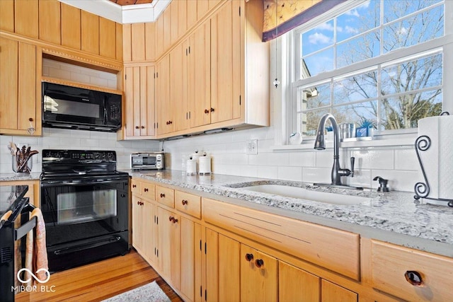 kitchen featuring light brown cabinetry, light stone counters, decorative backsplash, black appliances, and a sink