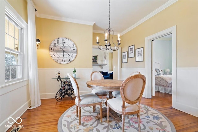 dining area featuring an inviting chandelier, ornamental molding, wood finished floors, and wainscoting