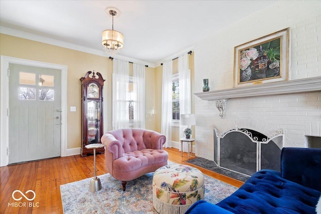 living area with ornamental molding, a brick fireplace, baseboards, and wood finished floors