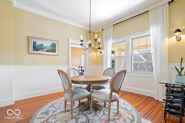 dining area featuring an inviting chandelier, wood finished floors, a wainscoted wall, and visible vents