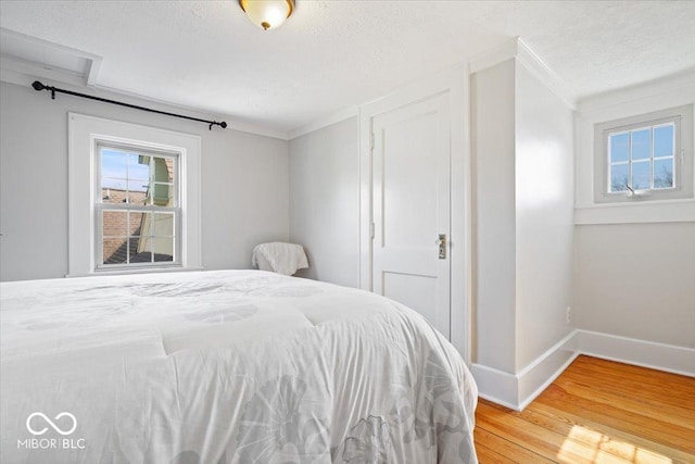 bedroom featuring baseboards, a textured ceiling, light wood-style flooring, and ornamental molding