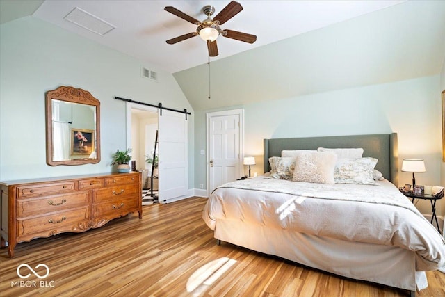 bedroom with a ceiling fan, wood finished floors, visible vents, lofted ceiling, and a barn door