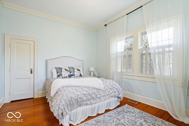 bedroom featuring visible vents, baseboards, wood finished floors, and ornamental molding