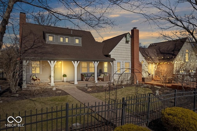 rear view of house featuring a fenced front yard, a lawn, a porch, and a chimney