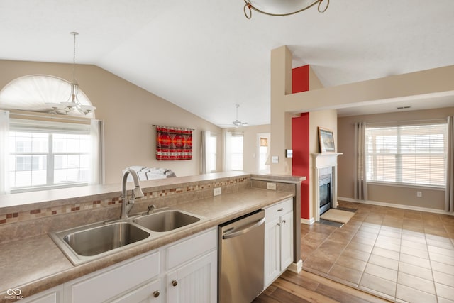 kitchen with a fireplace with flush hearth, a sink, white cabinetry, vaulted ceiling, and dishwasher