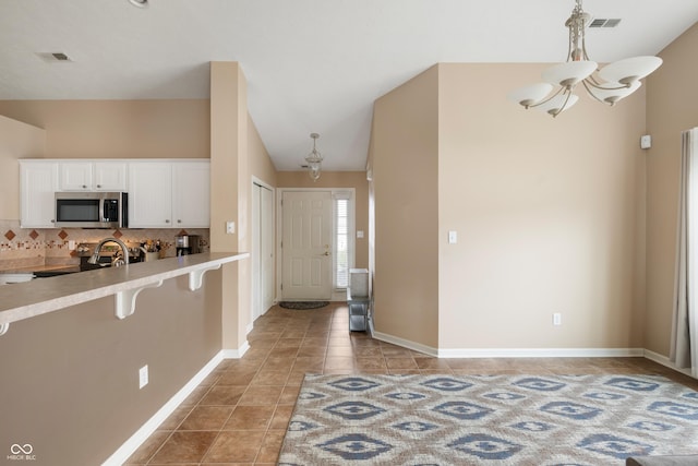 kitchen featuring a notable chandelier, light tile patterned floors, stainless steel appliances, backsplash, and white cabinets