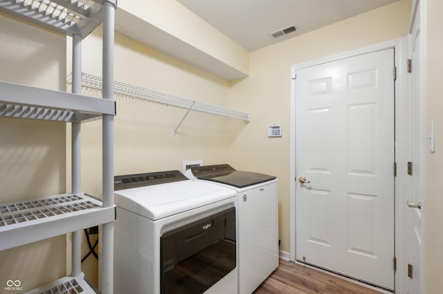 laundry room with laundry area, washing machine and dryer, visible vents, and wood finished floors