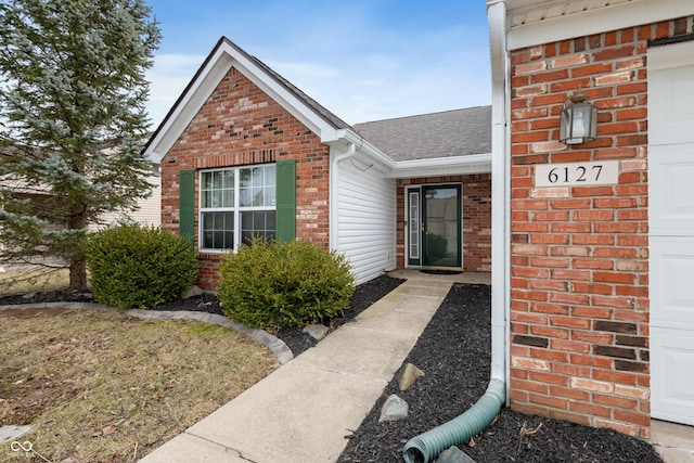 entrance to property featuring an attached garage, a shingled roof, and brick siding