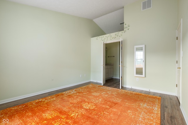 unfurnished bedroom with baseboards, visible vents, wood finished floors, ensuite bathroom, and vaulted ceiling