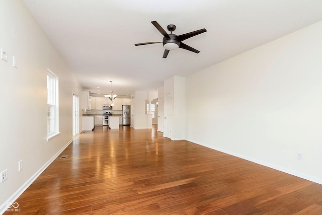 unfurnished living room featuring ceiling fan with notable chandelier, wood finished floors, and baseboards