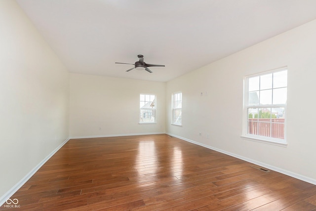 empty room with hardwood / wood-style floors, a ceiling fan, visible vents, and baseboards