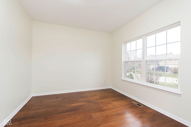 empty room featuring baseboards, visible vents, and dark wood-style flooring