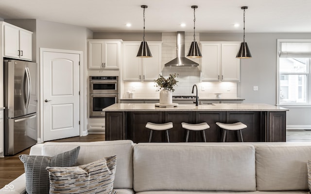 804 Whispering Oaks Dr, Carmel, IN 46032 - kitchen featuring stainless steel appliances, wall chimney exhaust hood, a kitchen island with sink, white cabinets, and dark wood finished floors