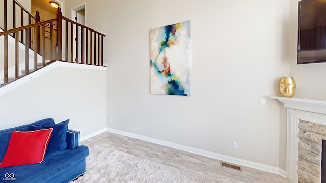 sitting room featuring a stone fireplace, wood finished floors, visible vents, baseboards, and stairs