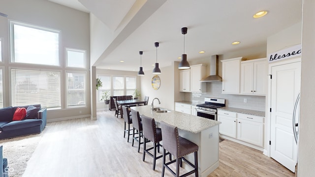 kitchen featuring decorative backsplash, wall chimney exhaust hood, stainless steel range with gas stovetop, a kitchen bar, and a sink