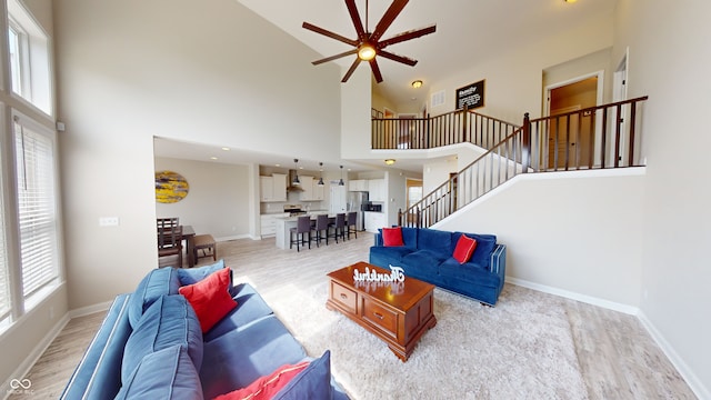 living area featuring a ceiling fan, light wood-style flooring, stairway, and baseboards