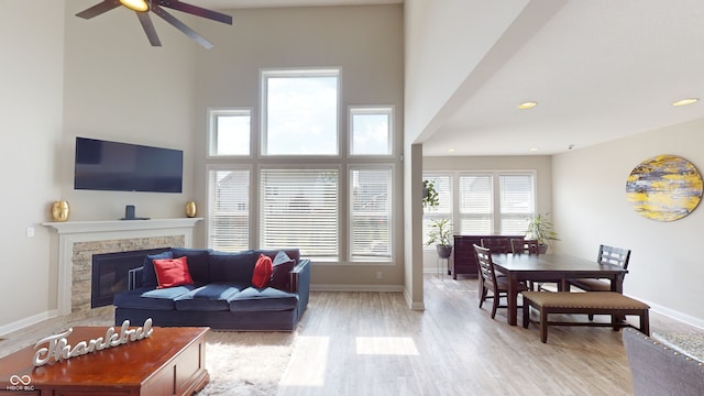 living room featuring recessed lighting, a high ceiling, baseboards, light wood finished floors, and a glass covered fireplace