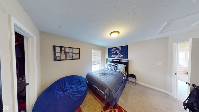 carpeted bedroom with a textured ceiling, attic access, and baseboards