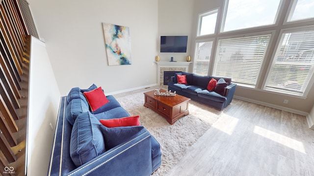 living area featuring a fireplace, stairway, a high ceiling, light wood-style flooring, and baseboards