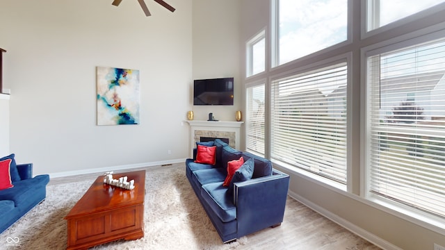 living room featuring a stone fireplace, wood finished floors, a ceiling fan, a towering ceiling, and baseboards